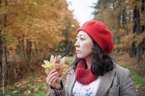 A sad looking asian girl wearing red beret. Looking in the past. Autumn mood.