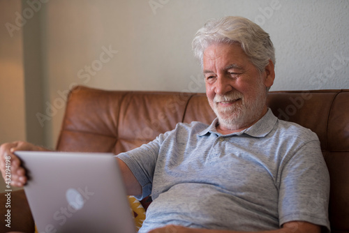 Happy aged man indoor working at laptop and smiling, relaxed senior male using computer browsing or surfing internet, reading news online, excited elderly people texting message at pc at home