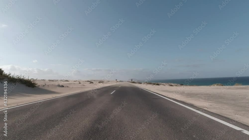 Pov driving car through sand dunes landscape by the sea with sand on the road. Corralejo, Fuerteventura, Canary Islands. Pov driving car through sand dunes landscape by the sea with sand on the road. Corralejo, Fuerteventura, Canary Islands.