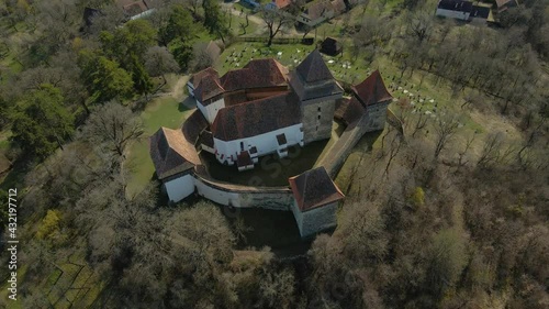 Aerial footage of a medieval fortified Church located in Viscri village, Brasov, Romania. Drone shot from a higher angle while lowering altitude and keeping the church in focus. photo