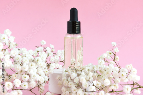 Cosmetic bottle with dropper on a pink background. Flowering branch of gypsophila. natural cosmetics concept and bernding.