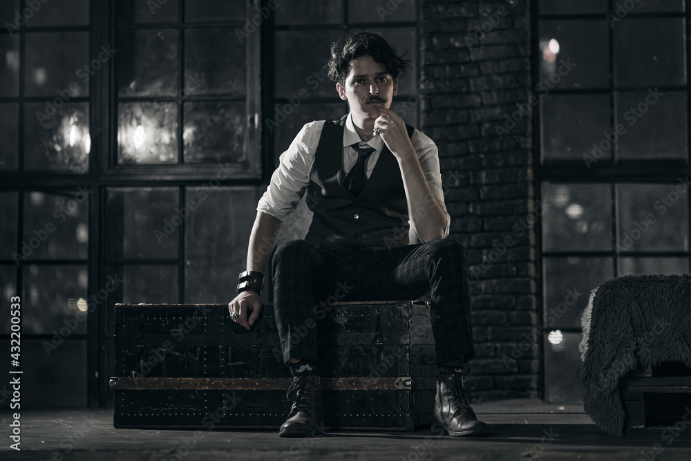 stylish dressed man stands at the window and looks into the distance. pensive man stands at night in a dark room stylish dressed man stands at the window and looks into the distance. pensive man stands at night in a dark room
