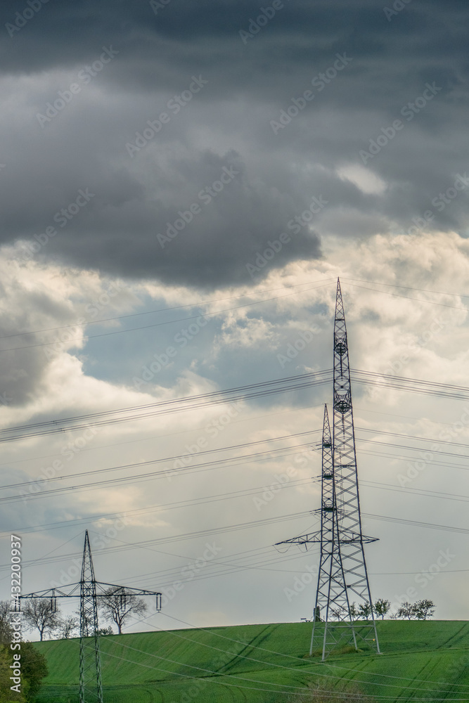 Strommasten einer Überlandleitung vor dunklem Wolkenhimmel