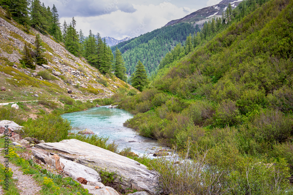 Walk to Lake Combal. Landscape at the Miage glacier, with the view of the river and the mountains, in summer, with cloudy sky. Italian Alps. Aosta Valley. Italy