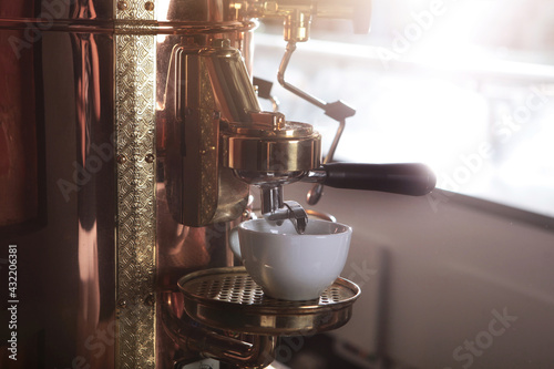 Large vintage copper coffee machine. Antique styling. White coffee cup. Free space.Sunlight.