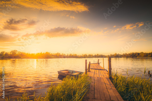 Sunset over the lake with a wooden bridge and boat. View from the shore