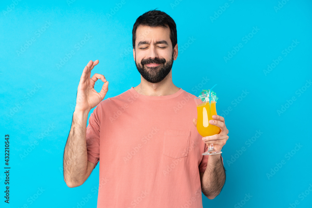 Young man over holding a cocktail over isolated blue background in zen pose Young man over holding a cocktail over isolated blue background in zen pose