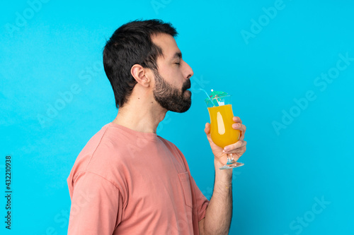 Young man over holding a cocktail over isolated blue background