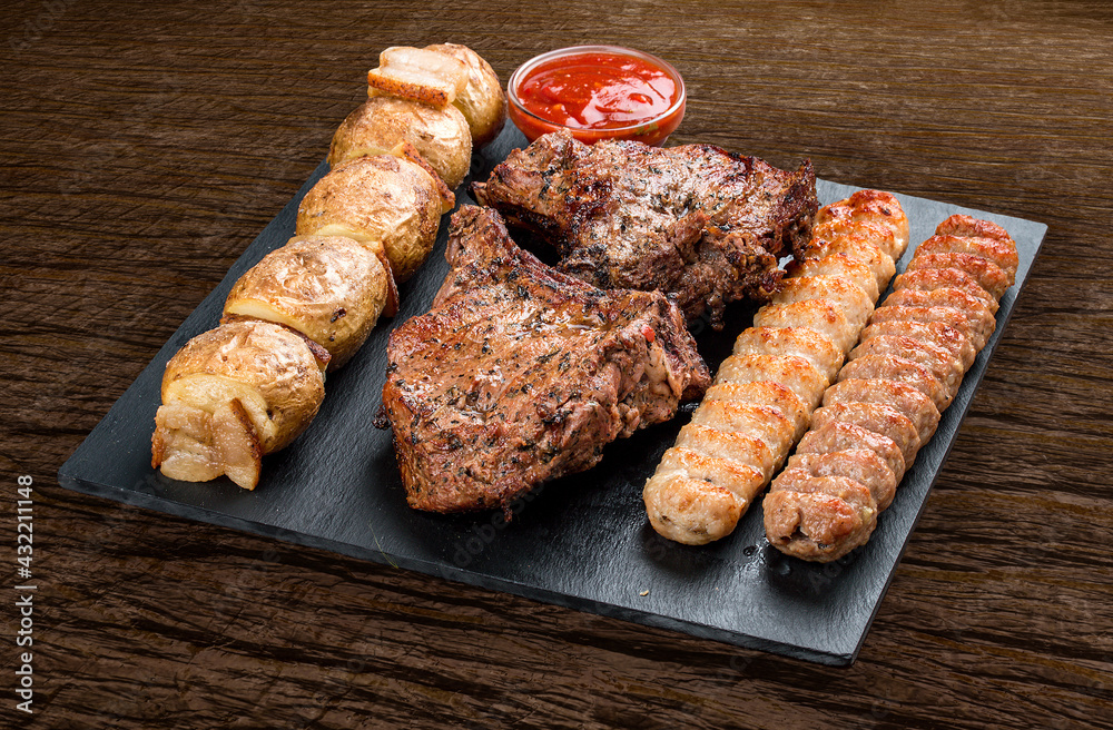 Stone board with different tasty cooked meat on wood background. Veal kebab, lyulya, potatoes.