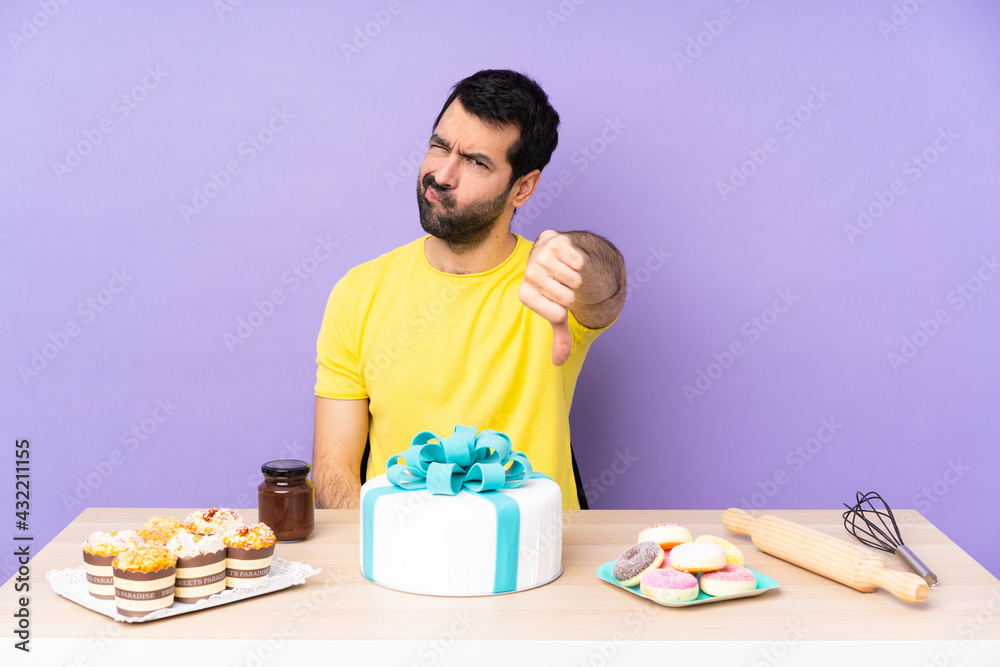 Man in a table with a big cake showing thumb down with negative expression Man in a table with a big cake showing thumb down with negative expression