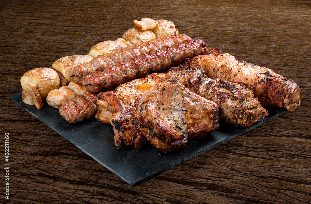 Stone board with different tasty cooked meat on wood background. Pork neck, potatoes, kebab