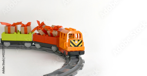 Colorful toy train with gifts on curve railway on white background. Childhood playing concept for preschool education, game or greeting birthday party. Plastic blocks. Banner.