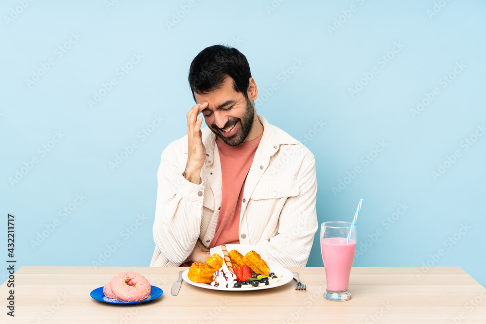 Man at a table having breakfast waffles and a milkshake laughing