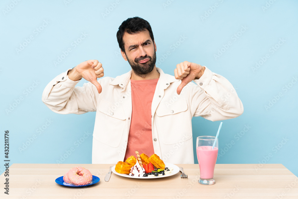 Man at a table having breakfast waffles and a milkshake showing thumb down Man at a table having breakfast waffles and a milkshake showing thumb down