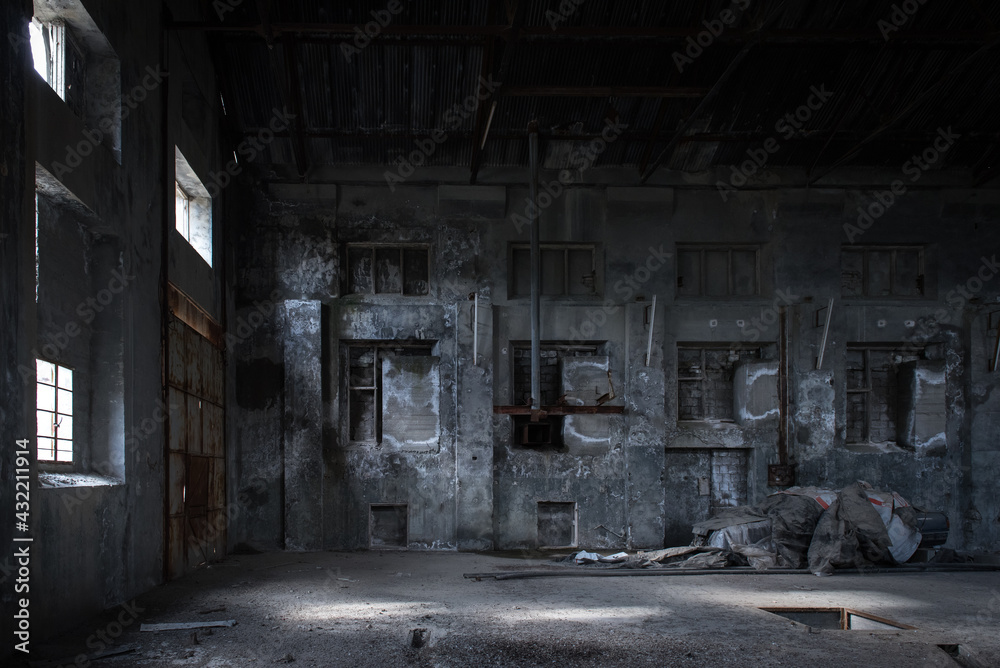 Industrial building backdrop. Interior of abandoned factory with stained concrete walls, bricked windows and pieces of old equipment 
