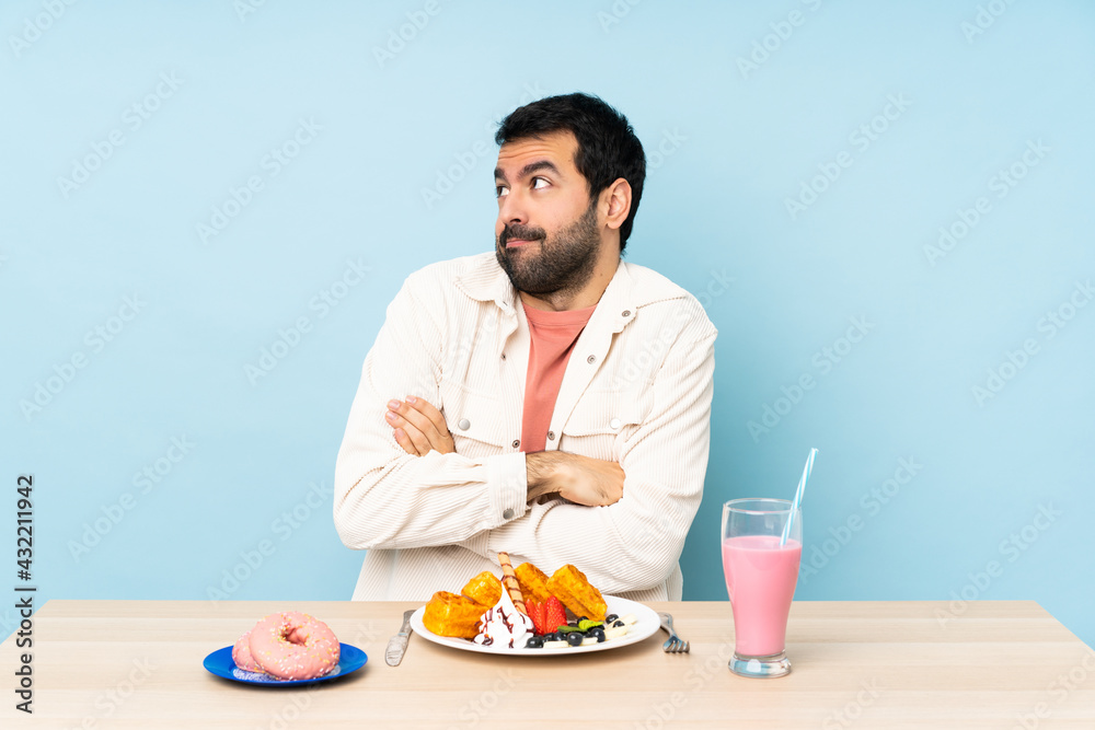 Man at a table having breakfast waffles and a milkshake making doubts gesture while lifting the shoulders Man at a table having breakfast waffles and a milkshake making doubts gesture while lifting the shoulders