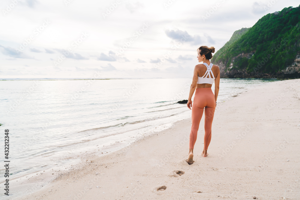Slim female walking along calm ocean in summer day