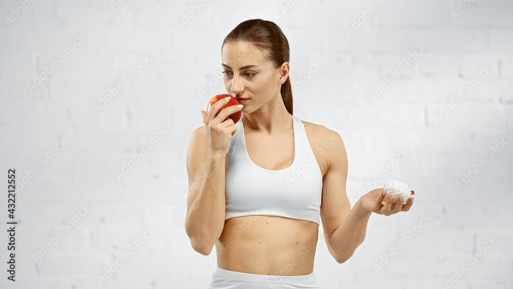 Fit sportswoman smelling apple and holding marshmallow. Fit sportswoman smelling apple and holding marshmallow.
