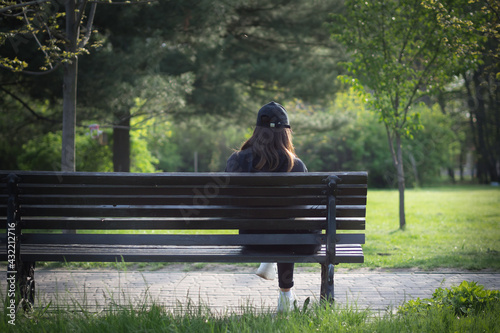 A lonely girl is sitting on a park bench. The face is hidden.