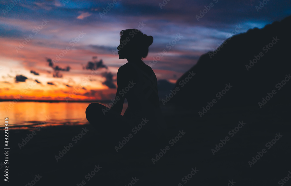 Silhouette of calm woman resting near ocean looking at horizon with colorful sky and getting inspiration from nature, tranquil female admire beauty of sea sitting at beach and dreaming on leisure