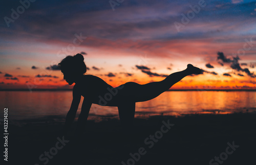 Silhouette of slim flexible woman stretching body during physical recreation at beach with colorful sky, fit girl doing asana poses training muscles for keeping healthy lifestyle and mental