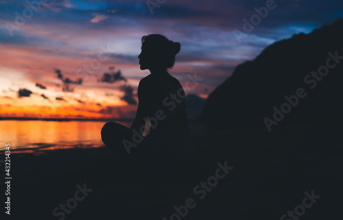 Silhouette of calm woman resting near ocean looking at horizon with colorful sky and getting inspiration from nature, tranquil female admire beauty of sea sitting at beach and dreaming on leisure