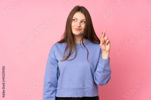 Teenager caucasian girl isolated on pink background with fingers crossing and wishing the best