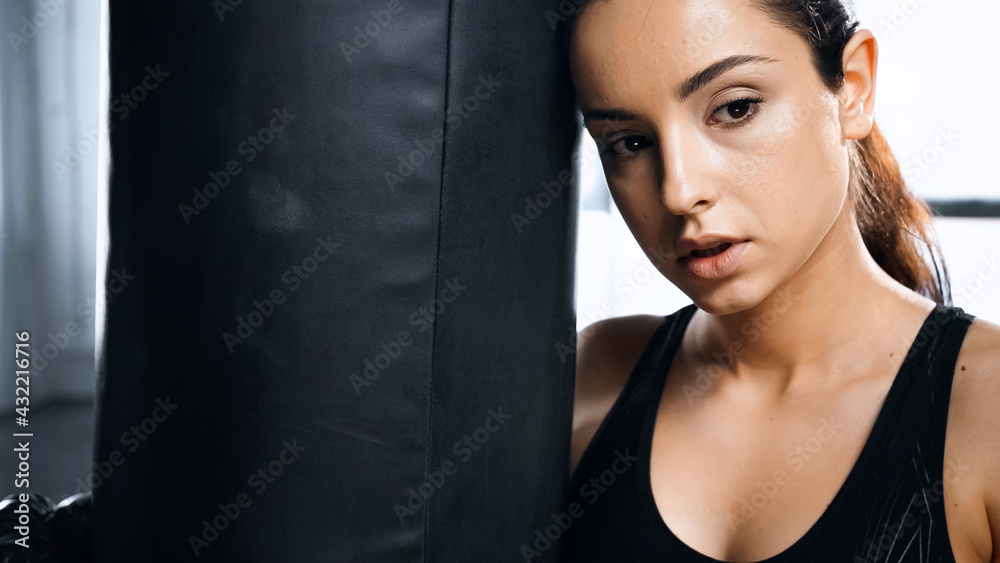 tired young sportswoman leaning on punching bag in gym.