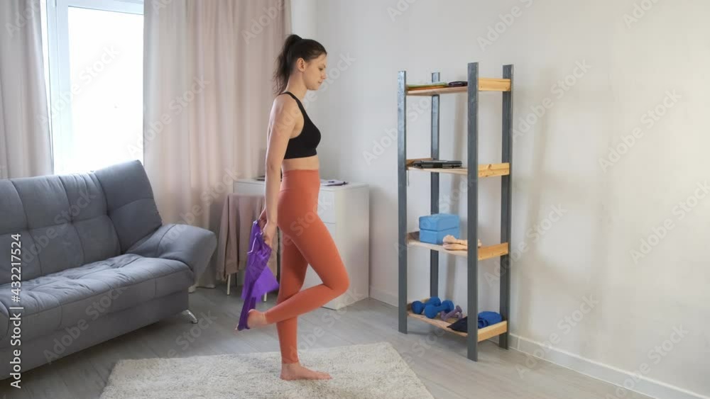 Young woman in sportswear is stretching leg and backbend with resistance band at home. She is improving posture and stability. Sport yoga fitness training stretching yoga and wellness concept. Young woman in sportswear is stretching leg and backbend with resistance band at home. She is improving posture and stability. Sport yoga fitness training stretching yoga and wellness concept.