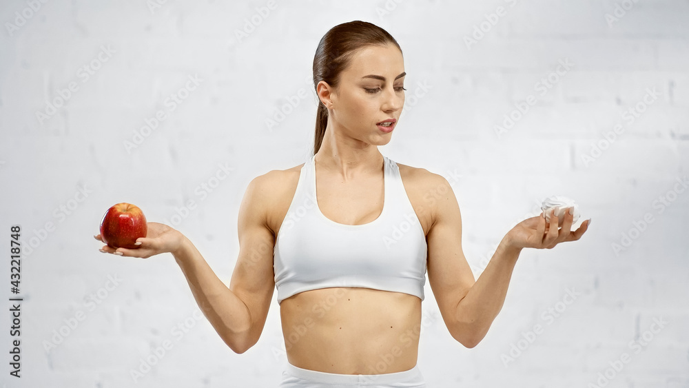 Sportswoman looking at marshmallow while holding apple. Sportswoman looking at marshmallow while holding apple.