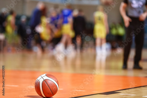 Basketball ball on the parquet with team and referee in the background. © Dziurek