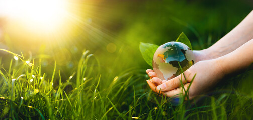 Hands holding crystal earth globe in sunny green grass.  Environment, save clean planet, ecology concept. Earth Day banner with copy space.
