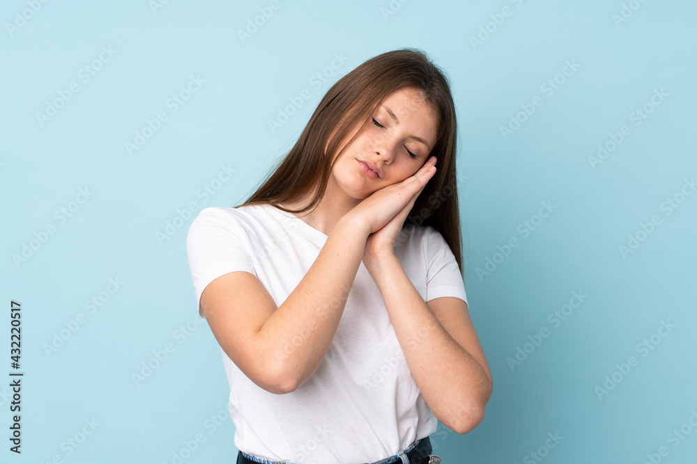 Teenager caucasian girl isolated on blue background making sleep gesture in dorable expression Teenager caucasian girl isolated on blue background making sleep gesture in dorable expression