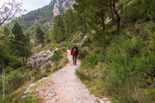 Hikers walking along a cobbled path, in a mountainous area surrounded by large rocky walls. In the Barranc del Cinc de Alcoy, Alicante (Spain)