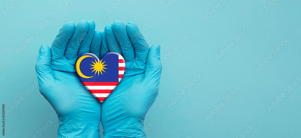 Fototapeta premium Doctors hands wearing surgical gloves holding Malaysia flag heart