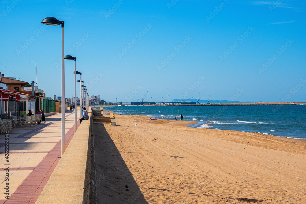 Daimuz beach, with clean and fine sand, on a sunny afternoon, with the port of Gandia in the background.