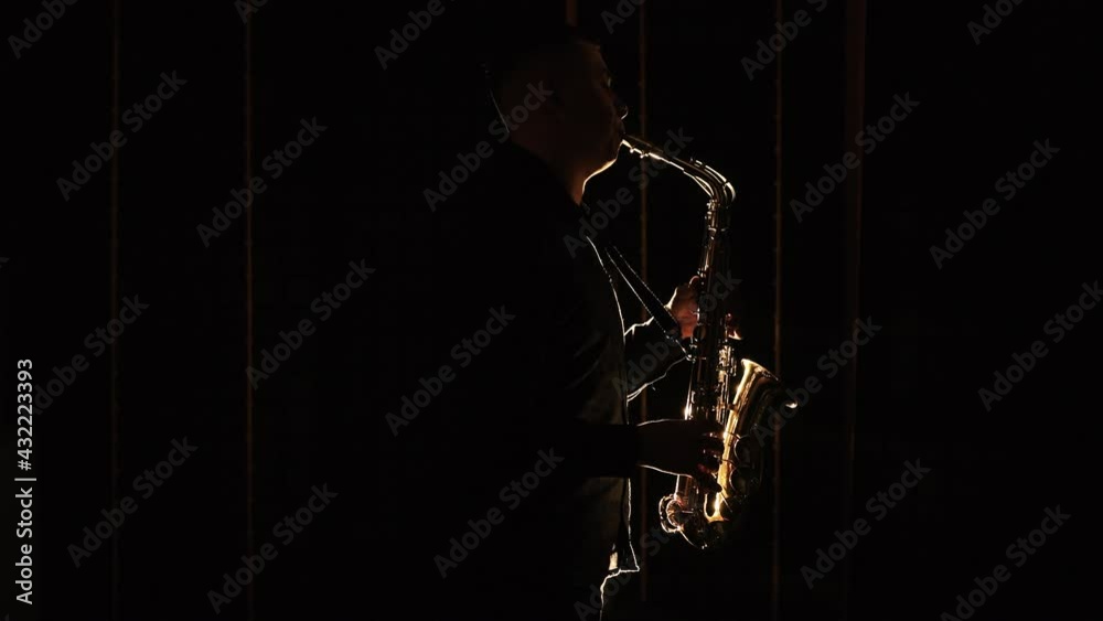 Black silhouette of male saxophonist musician playing golden alt saxophone on musical instrument. Cool saxophone player performing a solo on stage. Musician playing in band Black silhouette of male saxophonist musician playing golden alt saxophone on musical instrument. Cool saxophone player performing a solo on stage. Musician playing in band