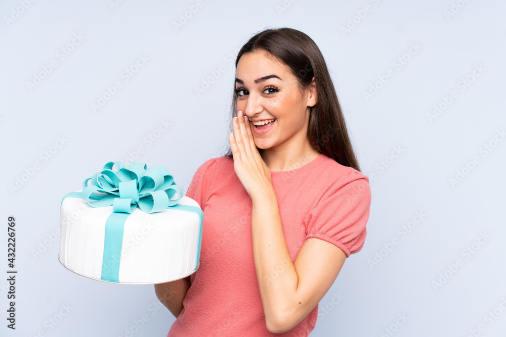 Pastry chef holding a big cake isolated on blue background whispering something Pastry chef holding a big cake isolated on blue background whispering something