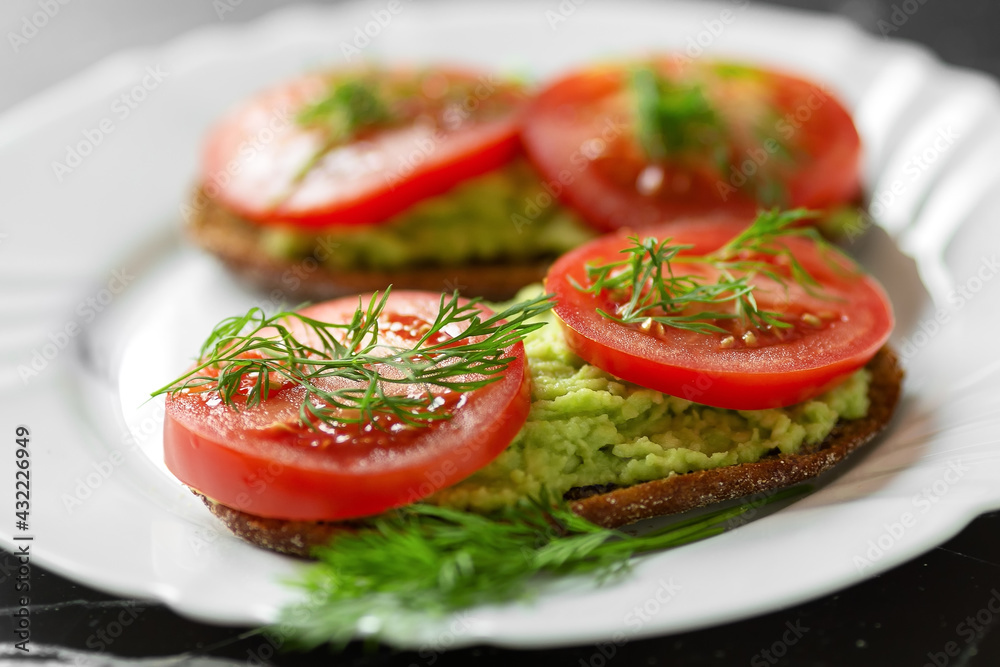 Sandwiches with grated fresh avocado and tomato slices on a white plate. Healthy eating. High quality photo