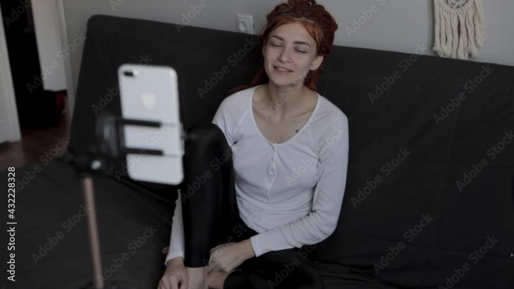 A woman blogger with red dreadlocks recording video or live broadcast using smartphone and tripod at home.Online show On-air production host streaming live content, recording digital social media A woman blogger with red dreadlocks recording video or live broadcast using smartphone and tripod at home.Online show On-air production host streaming live content, recording digital social media