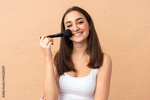 Young caucasian woman isolated on beige background holding makeup brush
