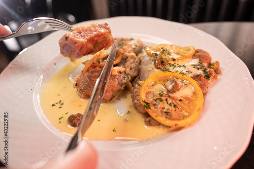 Woman hands cutting veal piccata served in a sauce using a fork and knife close-up, shallow focus