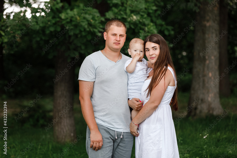 Happy young family, mom, dad and baby son spending time together outdoors in summer green garden