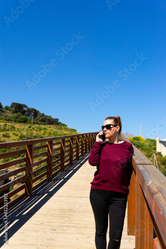 Mujer joven paseando y usando un smartphone en un puente de madera