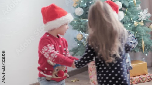 3 authentic happy Joy children round dance holding hands walk in circle by Christmas tree play have fun together. Preschool toddler kids celebrate New Year festive atmosphere. Winter, holiday concept