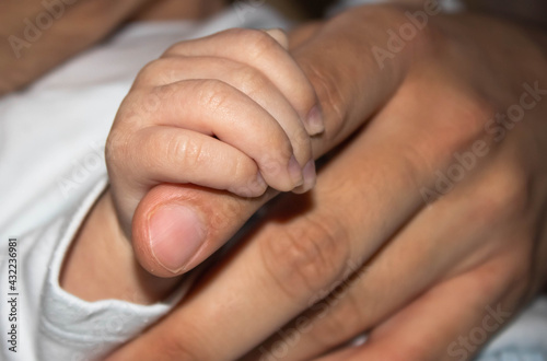 The baby's hand holds the father's index finger, concept of trust and safety