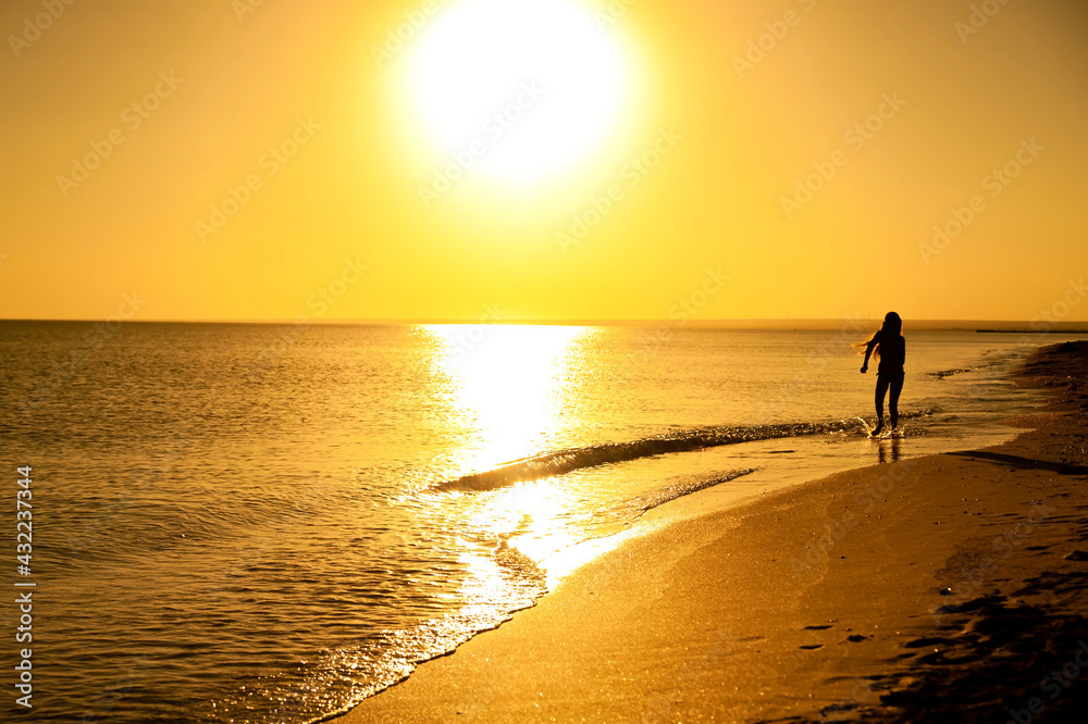 Silhouette of a girl running along the edge of the water in the sea at sunset. Recreation and sports concept