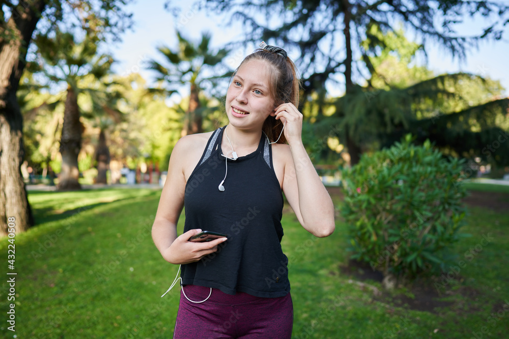 a beautiful red-haired girl with green eyes puts on your headphones to listen to her favorite music before exercising in a park near the city