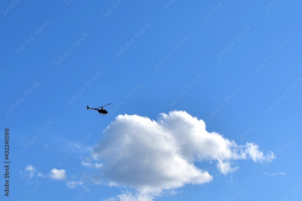 small silhouette of helicopter against big white cloud on blue sky small silhouette of helicopter against big white cloud on blue sky