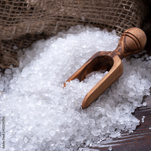 White sea salt for cooking food on a dark wooden table, natural spoon and coarse bag